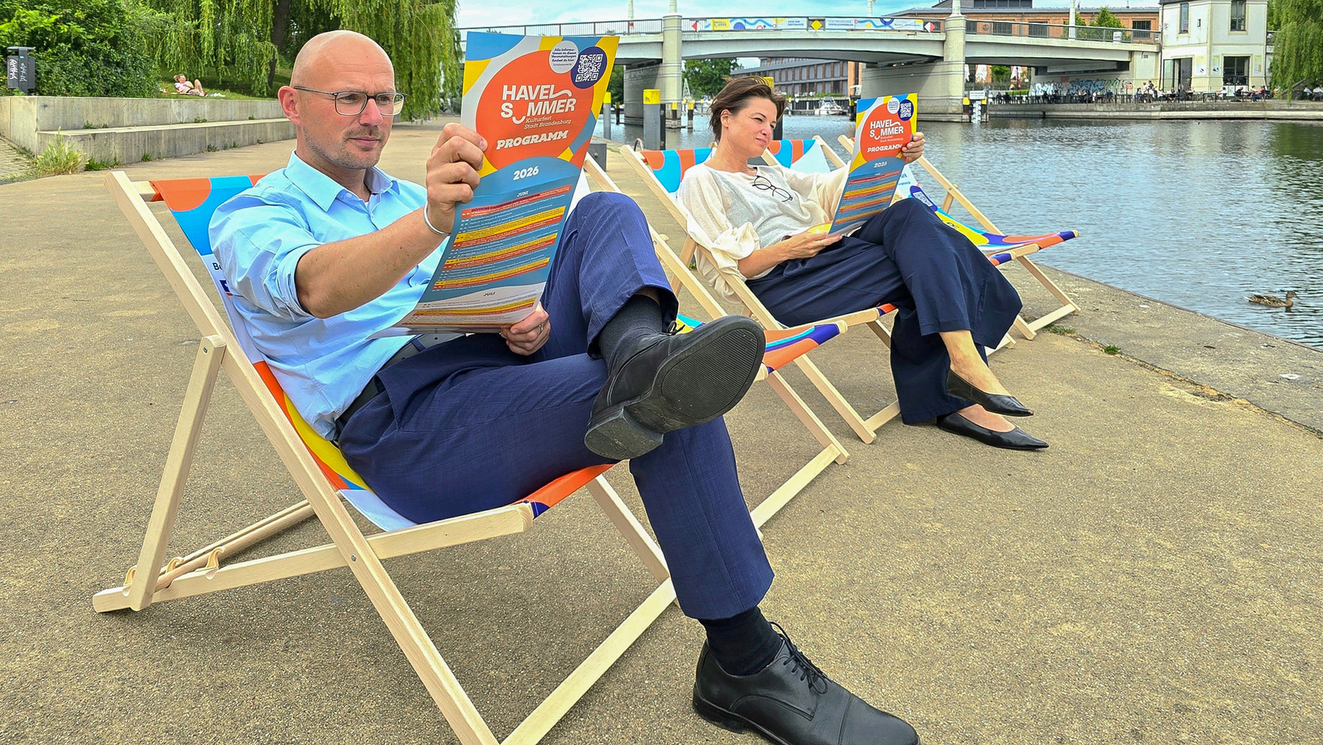 Oberbürgermeister Daniel Keip und Kulturbüro-Leiterin Stephanie Knitter haben schon mal die bunten Havelsommer-Liegestühle getestet und dabei im Havelsommer-Flyer geschmökert. Sie freuen sich auf den Havelsommer-Start am 7. Juni mit der Havelkarawane. © Stadt Brandenburg an der Havel / Th. Messerschmidt